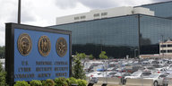 Blick auf die Zentrale der NSA in Fort Meade mit vollem Parkplatz und einer Tafel mit dem Wappen der NSA