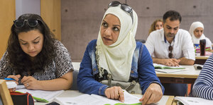 Zahra Alzaher sitzt in einem Klassenraum und legt, während sie hochschaut und nach links blickt, einen Finger auf eine Buchseite