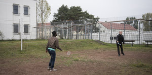 Zwei Männer spielen Federball über ein gespanntes Netz im Hof einer Haftanstalt