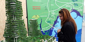 Frau steht vor Modell eines Öko-Hochhauses in Malaysia