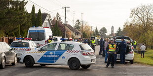 Polizisten stehen neben einem Polizeiauto, das quer über eine Straße geparkt ist