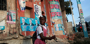 Ein Mädchen läuft vor einer Wand entlang, an der mit Wahlplakate hängen
