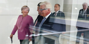 Merkel, Gabriel und Steinmeier laufen hinter einer Glasscheibe