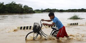 Ein philippinischer Junge schiebt sein Fahrrad durch knietiefes Wasser