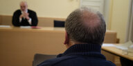 Ein Mann mit Halbglatze von hinten fotografiert, er sitzt in einem Gerichtssaal