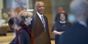 Barack Obama und Angela Merkel hinter einer Glasscheibe