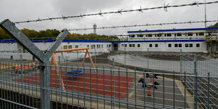 Ein Spielplatz und ein Wohncontainer hinter Stacheldraht