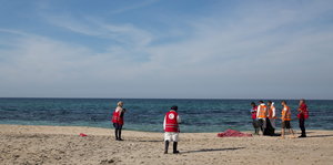 Mitarbeiter des roten Halbmondes mit der verdeckten Leiche eines ertrunkenen Flüchtlings am Strand