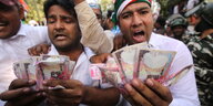 Zwei indische Männer in heller Kleidung halten Geldscheinbündel hoch
