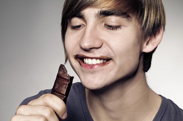 Ein junger Mann mit schokoladenverschmiertem Mund beißt grinsend in ein Stück Schokolade