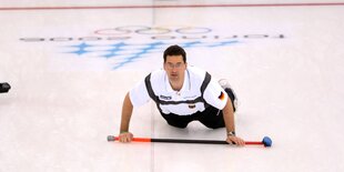 Ein Curlingspieler, beinahe auf dem Bauch liegend, mit aufmerksamen Blick