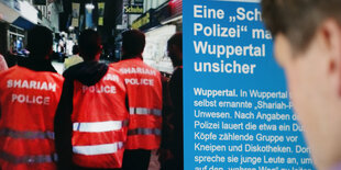 Drei Männer mit dem Rücken zur Kamera. Alle tragen sie Warnwesten mit der Aufschrift „Scharia-Polizei“