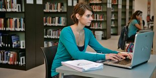 Eine Studentin arbeitet in einer Bibliothek mit ihrem Laptop.