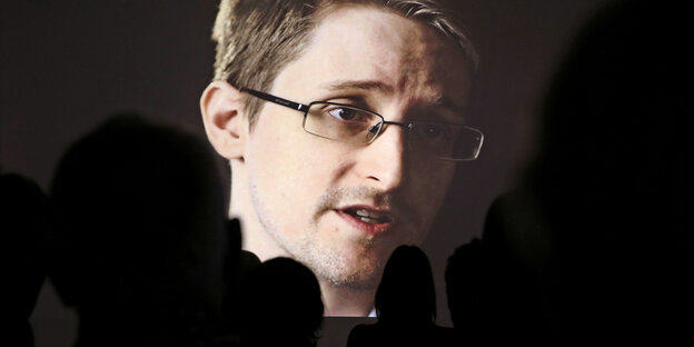 Edward Snowden auf einer Leinwand, im Vordergrund die Silhouetten von Zuschauern