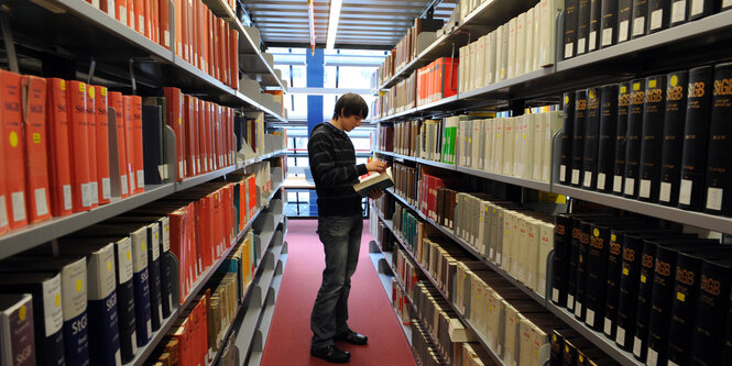 Ein Student liest zwischen den Regalen einer Uni-Bibliothek.