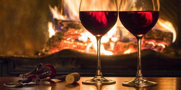 Zwei Gläser mit Rotwein vor einem Kamin