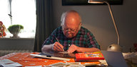 Ein älterer Herr malt an einem Tisch