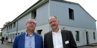 Zwei Männer stehen vor einem Haus aus Beton und Wellblech