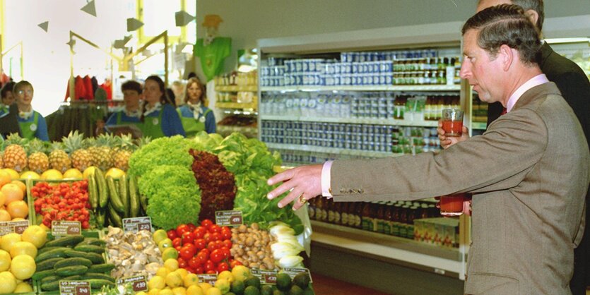 Prince Charles steht in einem Supermarkt vor einem Obstregal