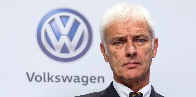 Älterer Herr mit weißen Haaren vor einer Werbewand mit VW-Logo