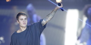 Justin Bieber hält ein Mikrofon in der linken Hand, die er in die Luft hebt