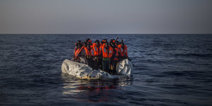 Menschen mit Rettungswesten auf einem Schlauchboot im Meer