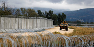 Ein gepanzertes türkisches Militärfahrzeug fährt an einer Mauer an der türkisch-syrischen Grenze entlang, im Vordergrund ist Stacheldraht zu sehen