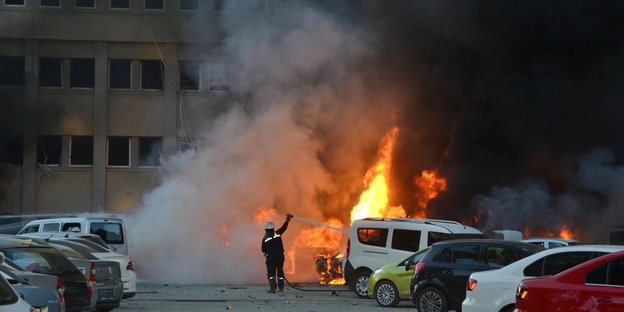 Ein Feuerwehrmann steht vor einer Rauchwolke und einem brennenden Auto und versucht, das Feuer zu löschen