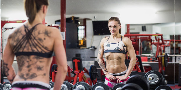 Eine Frau steht in einem Gym vor einem Spiegel und schaut sich an