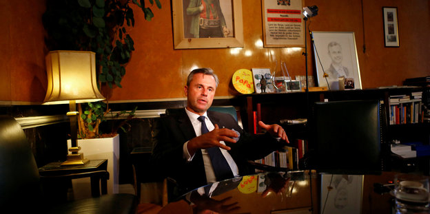 Der österreichische Politiker Norbert Hofer sitzt an einem Tisch in einem vollgestellten Büro