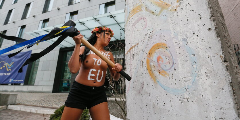 Eine halbnackteFrau schlägt mit einem Vorschlaghammer auf einen teil der Berliner Mauer vor der deutschen Botschaft in Kiew ein