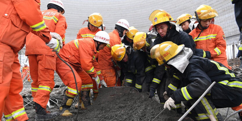 Männer in orange- und dunkelfarbenen Anzügen auf einer Baustelle