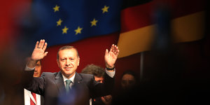 Recep Tayyip Erdoğan winkt mit beiden Händen. Im Hintergrund eine Europafahne
