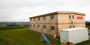 Ein Holzhaus, die wiederaufgebaute Flüchtlingsunterkunft in Altenfelden, steht auf einem Hügel vor dem Ausblick in die Landschaft