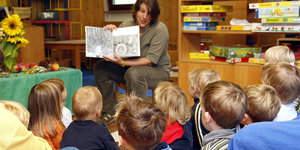 Eine Erzieherin in Kita zeigt Kindern ein Buch