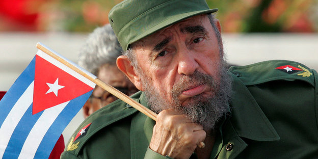 Ein Mann in Armeekleidung. Er hält die Miniaturflagge Kubas in der Hand