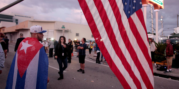 Menschen auf einer Straße, mit kubanischer und US-amerikanischer Flagge