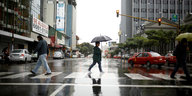 Eine Frau geht im Regen mit Schirm über die Straße