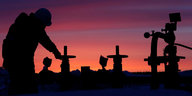 Silhouette eines Mannes und Ölfördermaschinen vor dramatischem Morgen- oder Abendrot