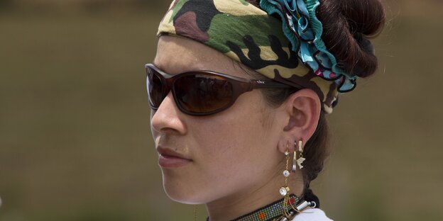 Eine Frau trägt eine Sonnenbrille und ein Camouflage-Stirnband Eine Frau trägt eine Sonnenbrille und ein Camouflage-Stirnband