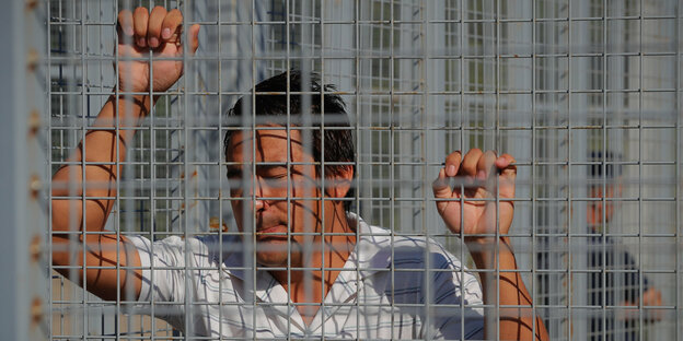 ein Mann hält sich an einem Gitterzaun fest