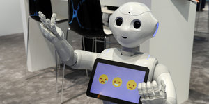 Ein Roboter hält ein Tablet, auf dem drei Smileys zu sehen sind