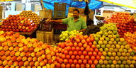 Ein indischer Händler sitzt hinter Bergen von Äpfeln und Zitronen