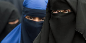 Drei vollverschleierte Frauen stehen nebeneinander. Zu sehen sind unter dem Niqab nur ihre Augen
