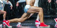Die nackten Beine eines Balletttänzers in kurzer, silberner Hose und roten Turnschuhen