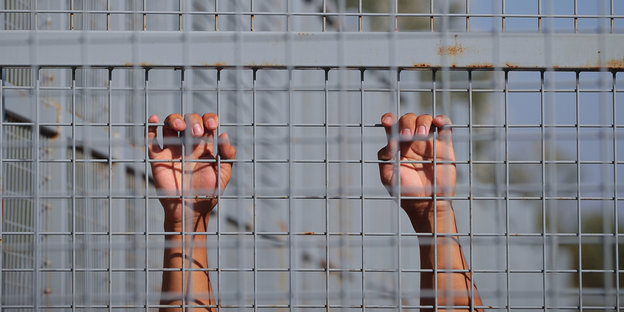 Eine Person klammert sich an die Gitterstäbe des Grenzzauns zu Ungarn