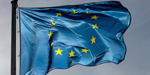 Die Flagge der EU weht vor dunkelgrauem Himmel