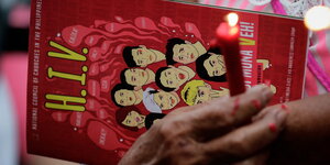 Frauenhände halten eine rote Kerze und eine Broschüre über HIV