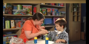 Eine Frau und ein Junge sitzen an einem Tisch, dahinter ein Regal voller Spiele