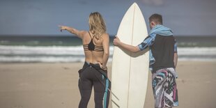 Zwei Leute mit einem Surfbrett am Strand